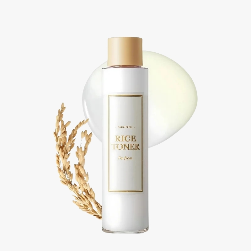 White cylindrical bottle with a gold cap labeled Rice Toner, flanked by rice stalks for a skincare product look. (informative)