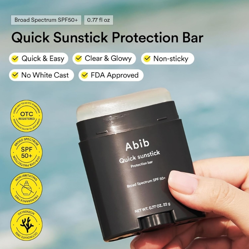 Sunstick sunscreen in hand with black container reading 'Abib Quick sunstick' against beach backdrop; SPF 50+ listed on label and product benefits shown as badges: quick & easy, clear & glowy, non-sticky, no white cast, FDA approved, broad spectrum.