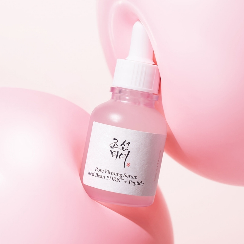 Pink glass dropper bottle of pore-firming serum labeled 'Pore Firming Serum, Red Bean PDRN + Peptide,' nestled among soft pink balloons.
