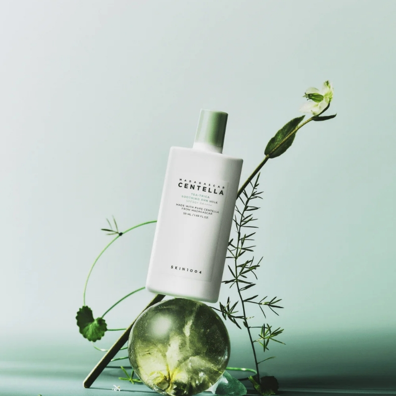 White skincare bottle labeled Madagascar Centella with a green cap, propped beside greenery and a glass orb on a mint background?