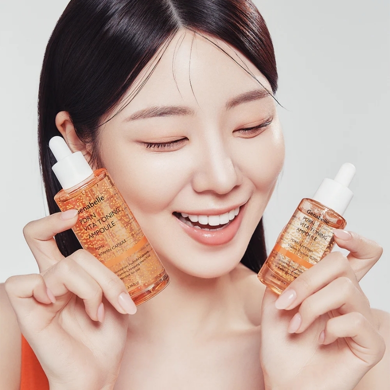 Smiling woman holding two orange Vitamin C serum bottles with droppers close to her face.