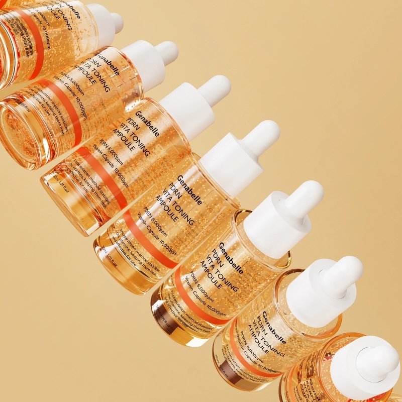 Row of orange serum dropper bottles arranged diagonally on a warm beige background, highlighting skincare ampoules.