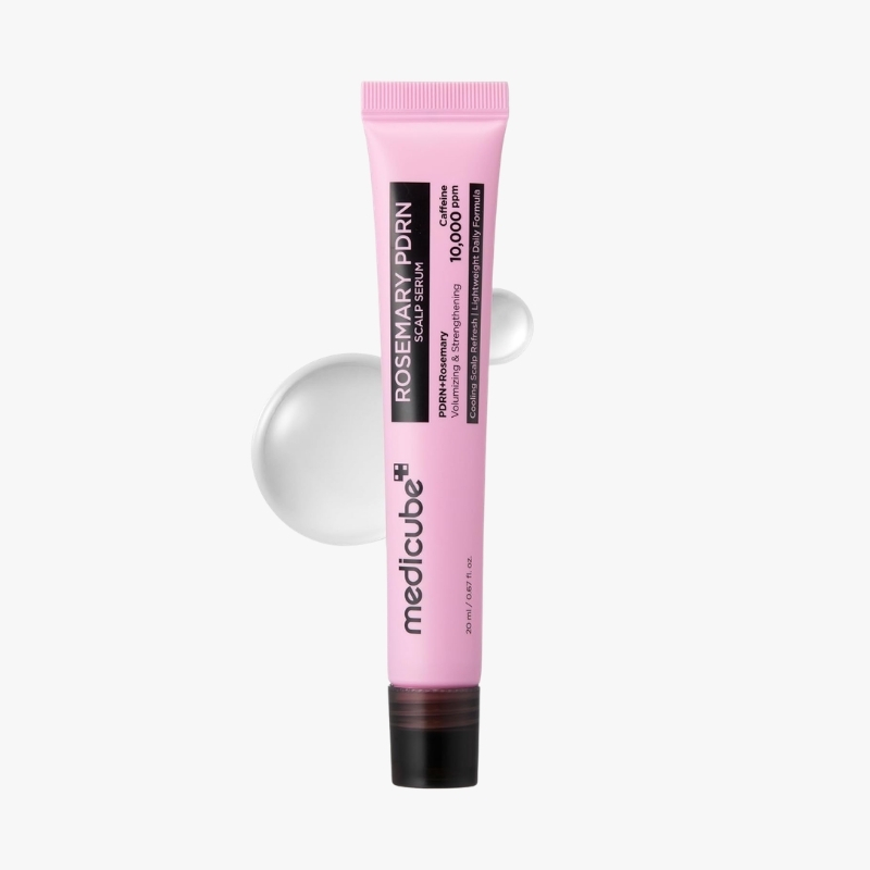 Pink tube of MedCube scalp serum standing upright with a black label; pink cap and a clear gel drop in the background, conveying a cosmetic scalp treatment.