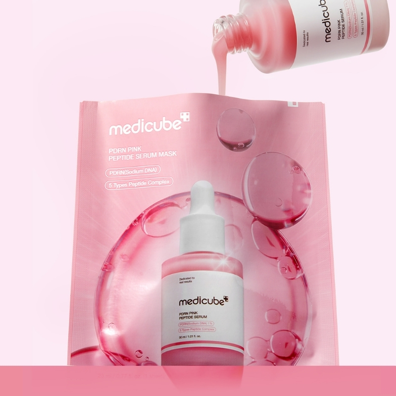 Pink Medcube serum kit with a droplet bottle in front of a pink facial mask packet; serum pours from a bottle above the scene.