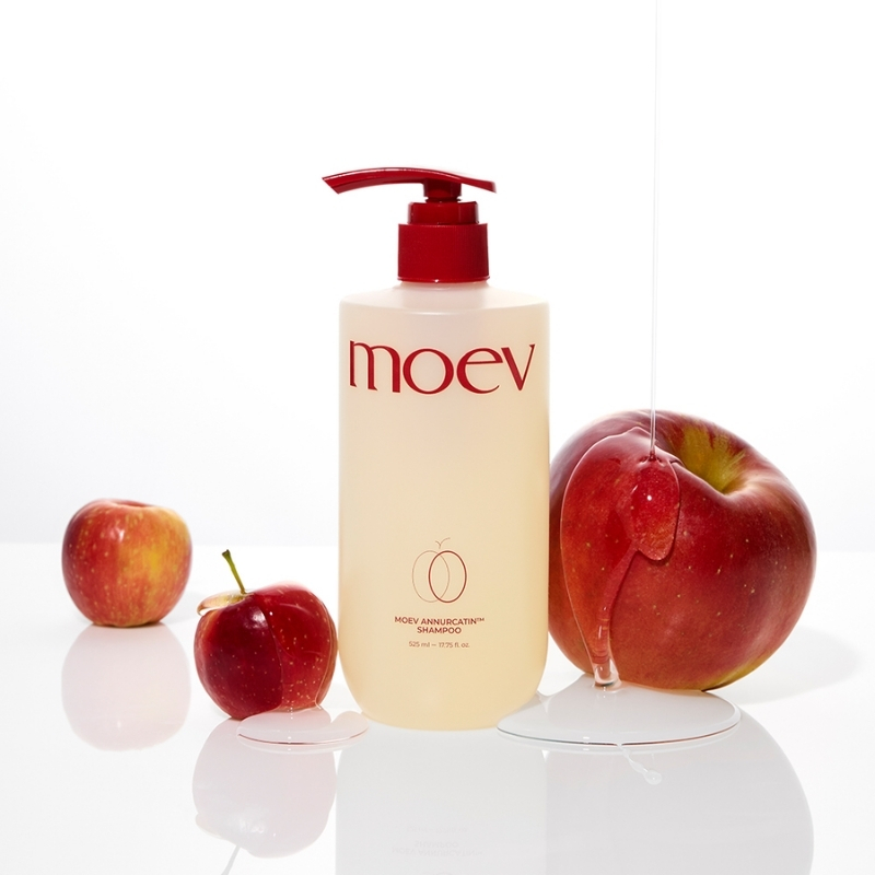 Moev shampoo bottle with red pump on a white surface, surrounded by red apples.